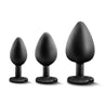 Set of three black silicone butt plugs in progressive sizes, perfect for anal training. Each plug features a tapered tip, bulbous body, thin neck, and heart shaped base with a white gem for safety and decoration. Additional images show alternate angles.