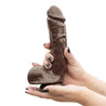 Chocolate skin tone ultra realistic dildo. Featuring a defined rounded head, subtle veins along the straight but flexible shaft, and realistic balls. Suction cup base. Additional images show alternate angles.